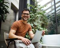 Junger mann sitzt am Laptop, im Hintergrund sind viele Pflanzen 