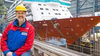 Erwin Sieems sitzt vor einerm Schiff in der Werft