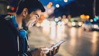 Lächelnder Mann mit Smartphone an nächtlicher Straße
