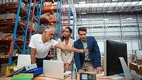 Zwei Männer und eine Frau besprechen sich in einer Lagerhalle